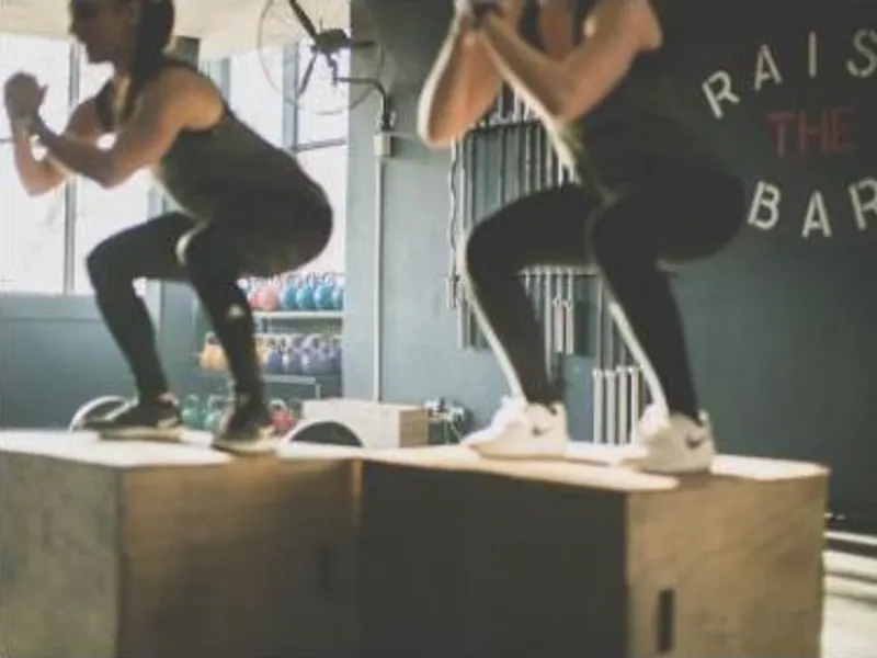 Two people doing box jumps at a gym