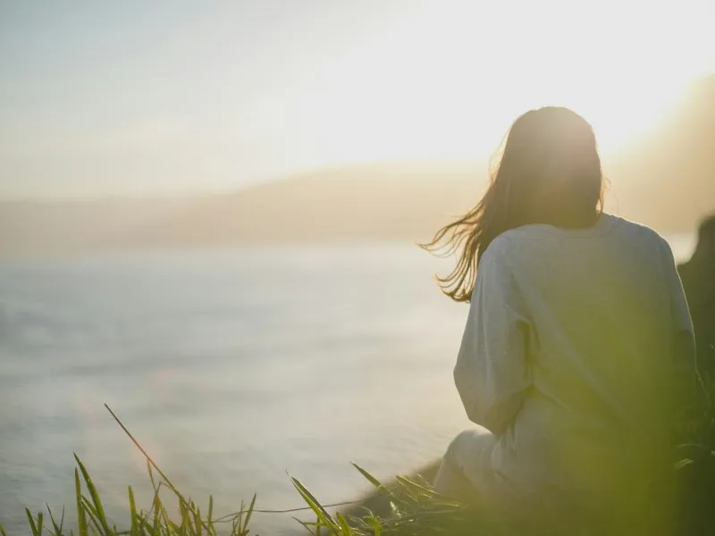 Mujer sentada en una roca mirando al mar en calma